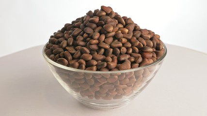 Pine nut rotate are on a table in a plate. Snack in transparent dish on an isolated white...