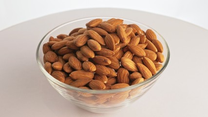 Nuts almond rotate are on a table in a plate. Snack in transparent dish on an isolated white background are spinning moving. Delicious and healthy protein-rich diet food.
