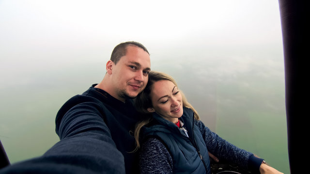 Adventure love couple on hot air balloon watermelon. Man and woman kiss hug love each other. Burner directing flame into envelope. Fly in morning blue sky. Happy people take selfie in hot air ballon.