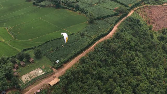 Amazing aerial video of flying paraglider on the background of wild nature. Paraplan drifting above the green tropical trees. Extreme sport. Hipster modern hobby concept. Paraplane flying in the sky.