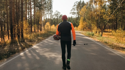Training an athlete on the roller skaters. Biathlon ride on the roller skis with ski poles, in the helmet. Autumn workout. Roller sport. Adult man riding on skates.The athlete goes and holds sports