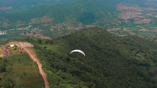 Amazing aerial video of flying paraglider on the background of wild nature. Paraplan drifting above the green tropical trees. Extreme sport. Hipster modern hobby concept. Paraplane flying in the sky.