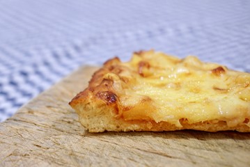 One single slice of cheese and pineapple pizza on top of a wooden cutting board