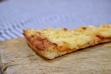 One single slice of cheese and pineapple pizza on top of a wooden cutting board