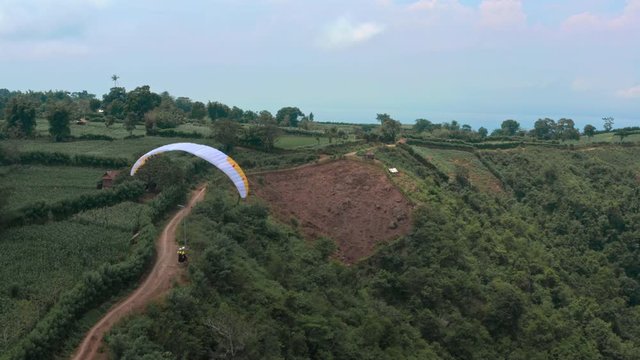 Amazing aerial video of flying paraglider on the background of wild nature. Paraplan drifting above the green tropical trees. Extreme sport. Hipster modern hobby concept. Paraplane flying in the sky.