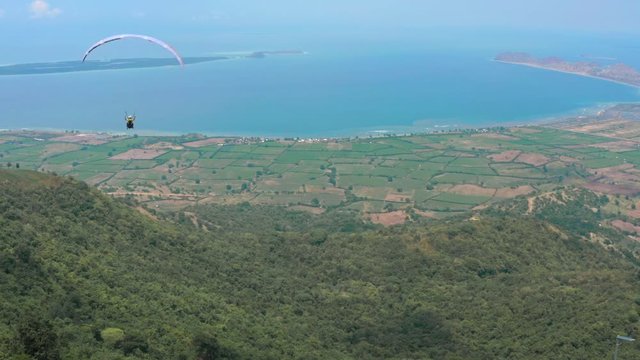 Amazing aerial video of flying paraglider on the background of wild nature. Paraplan drifting above the green tropical trees. Extreme sport. Hipster modern hobby concept. Paraplane flying in the sky.
