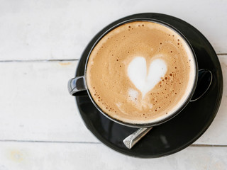 Heart shaped latte in a coffee cup black. Placed on a white wooden table.