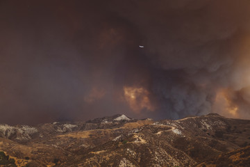 Blazing California wildfire with firefighter plane in dark smoke