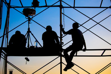 The staffs are on the crane at the outdoor concert construction with the sky in the evening or early morning , silhouette style.