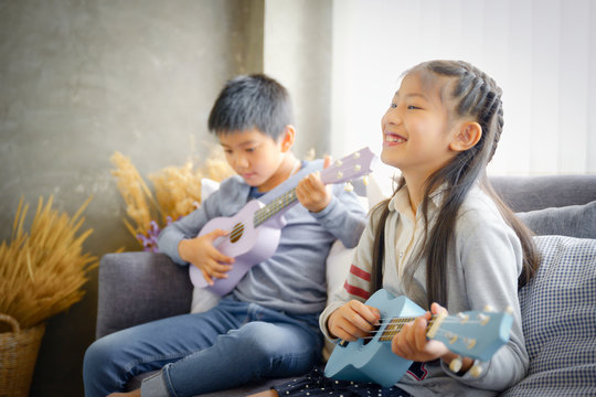 Happy elementary age Asian little kid is smiling  while playing a ukulele during a private music learning lesson at home