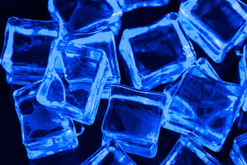 Ice cubes on black background with blue backlight. Illuminated ice cubes.  Macro horizontal photography
