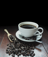 white cup of coffee with wooden spoon full of coffee beans on the table