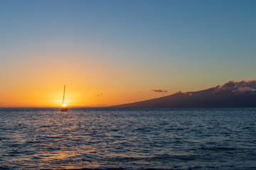 Fototapeta premium Lone boat anchored out at sea with islands in the background during sunset.