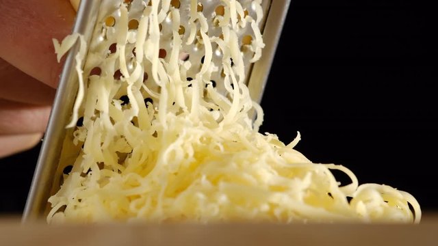 Cheese is being grated on the wooden board. Chef grating hard cheese. closeup black background
