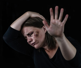 Crying woman victim of domestic violence and abuse showing a stop sign with her hand. Isolated on dark background