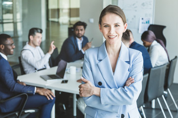 Fototapeta premium Business woman stands on the background of partners. A team of young businessmen working and communicating together in an office. Corporate businessteam and manager in a meeting