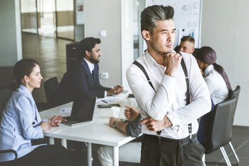 Business man stands on the background of partners. A team of young businessmen working and communicating together in an office. Corporate businessteam and manager in a meeting.