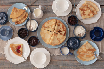 Shrovetide (Maslenitsa) - breakfast with blini stack, jam and sour cream with tea or coffe on bare plates on a wooden table.
