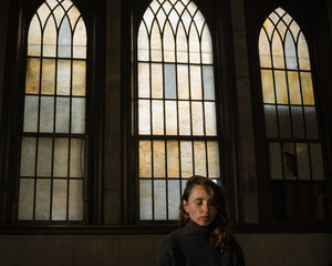 A young woman sits in a church with beautiful old stained glass