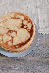 Cooking pancakes. Shrovetide (Maslenitsa) - blini stack on a blue plate on a wooden table.