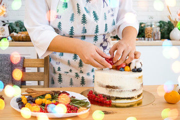 Cake decoration with lingonberry berries, blueberries and cotton. Women's hands in a frame in a bright kitchen. Christmas treat for the holiday. Lights of garlands.