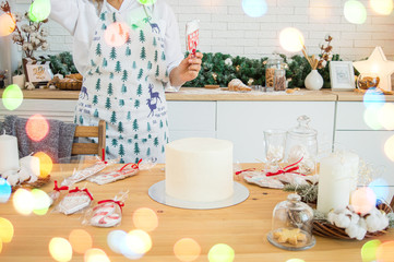 Cake decoration female hands in the frame in the bright kitchen gingerbread houses Christmas treat for the holiday lights of garlands