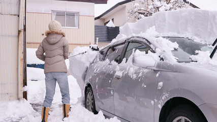 スノーワイパーで自動車の屋根の雪を降ろす女性