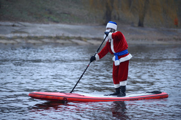 Man dressed like Santa Claus rowing SUP board on the river