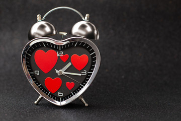 Steel clock alarm in the form of a heart with red hearts inside on a black glitter shiny...