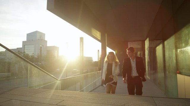 SLOW MOTION, CLOSE UP, LENS FLARE: Young business partners chat while walking through sunlit finance district. Successful businesswoman and male colleague talk while walking home from work at sunset.