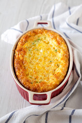 Homemade Cheddar Corn Pudding Casserole on a white wooden background, low angle view. Close-up.