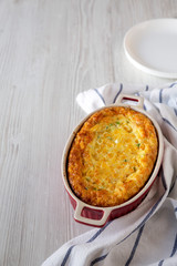 Homemade Cheddar Corn Pudding Casserole on a white wooden background, side view. Copy space.