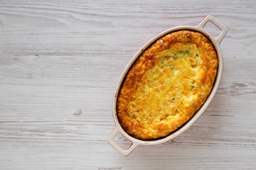 Homemade Cheddar Corn Pudding Casserole on a white wooden background, overhead view. Flat lay, top...