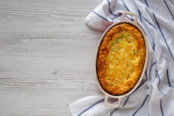 Homemade Cheddar Corn Pudding Casserole on a white wooden table, overhead view. Flat lay, top view, from above. Space for text.