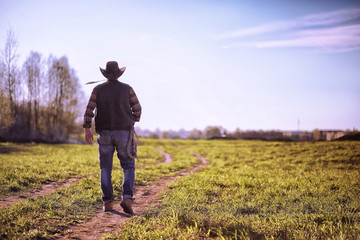 Cowboy standing in a field at sunset