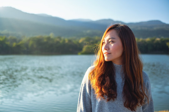 Portrait image of a beautiful asian woman standing in front of the lake and mountains before sunset