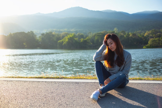 Portrait image of a sad woman sitting in front of the lake and mountains before sunset
