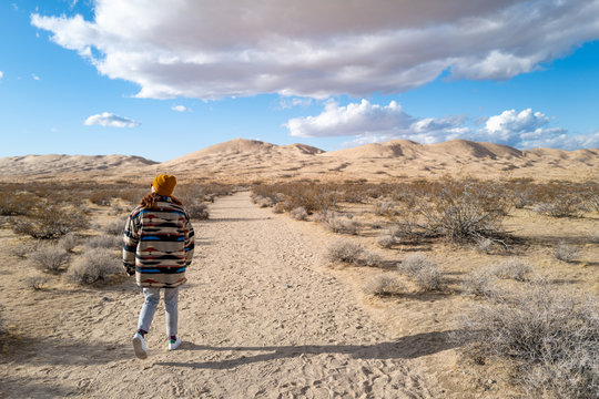 A young woman in a Native American patterned vintage jacket and mustard hat explores sand dunes in California