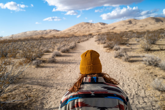 A young woman in a vintage Native American patterned jacket and mustard hat explores sand dunes in California