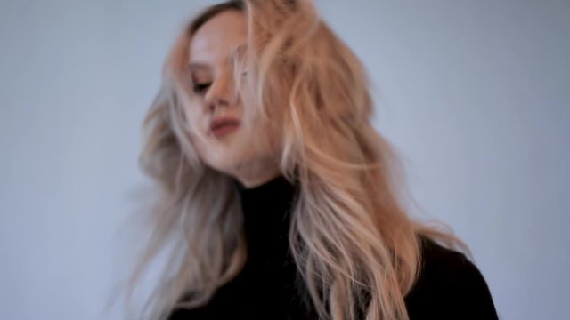 Charming blonde in a black turtleneck with sloppy curls, close-up dancing and shaking her head from side to side
