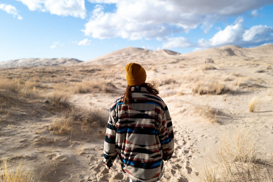 A young woman in a vintage Native American patterned jacket and mustard hat explores sand dunes in California