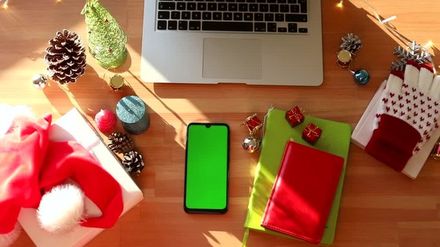 Top view of wooden desk with chroma key smartphone and Christmas decoration interior. Happy New Year. Winter holidays celebration. Family internet greeting gift. Green screen mockup. Sunlight. Sunny.