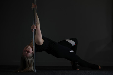 Fototapeta na wymiar The dancer on the pylon in the studio. Girl doing exercises on a sports equipment.