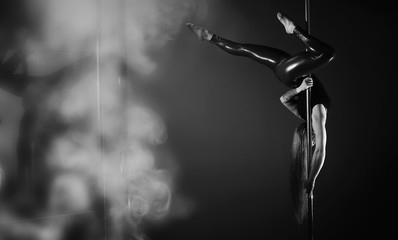 The dancer on the pylon in the studio. Girl doing exercises on a sports equipment.