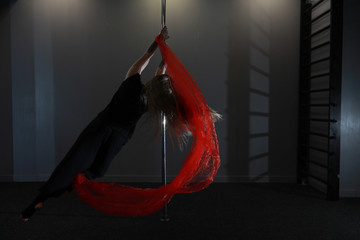 The dancer on the pylon in the studio. Girl doing exercises on a sports equipment.