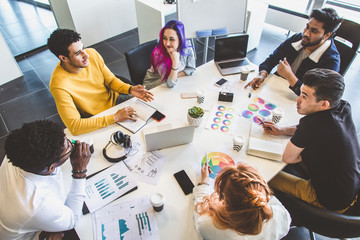 Group of multi ethnic executives discussing during a meeting. Business man and woman sitting around table at office and smiling. A team of young creative designers