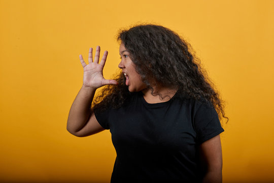 Young woman with overweight showing palm at camera, screaming over isolated orange background wearing fashion black shirt. People lifestyle concept.