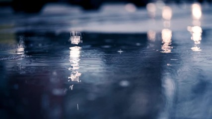 Closeup of puddle in Munich. Raindrops falling and blurry cars driving in background. Wet refelction on ground. Urban scene. - Powered by Adobe