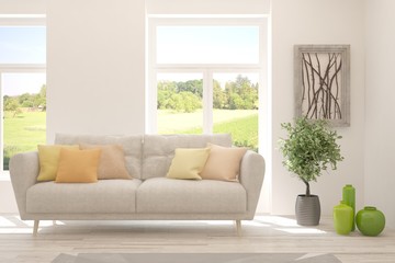 Fototapeta premium Stylish room in white color with sofa and summer landscape in window. Scandinavian interior design. 3D illustration