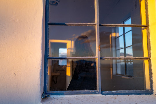 A woman walks in a motel window in a desert ghost town at sunset